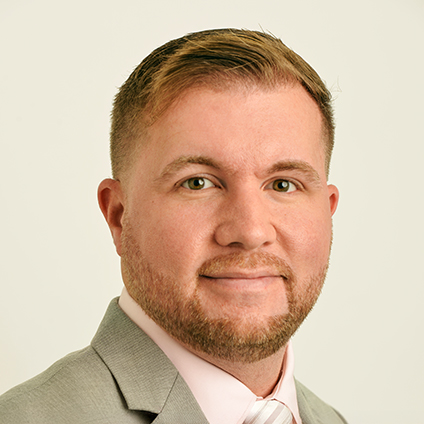 Head shot of a blond men with green eyes wearing a grey suit and pink shirt
